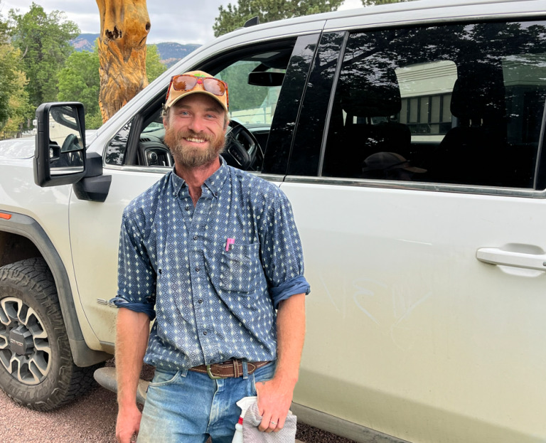 Will Frost, in a cap and a blue plaid shirt, smiles beside a white pickup truck