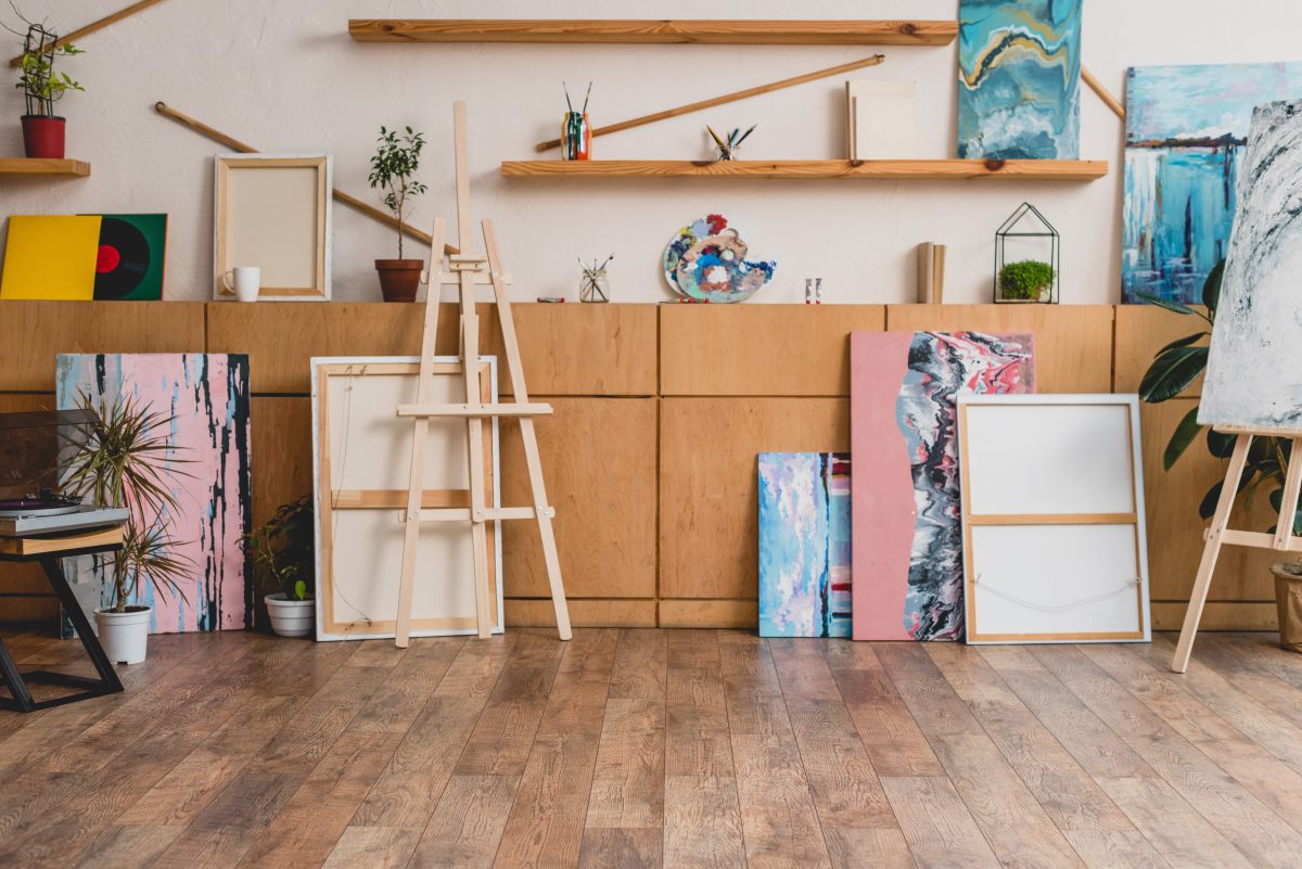 A bright art studio with a wooden easel, a blank framed canvas, potted plants and a vinyl record on a wood counter